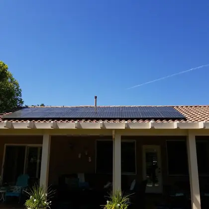 Solar panels along a tile roof above a shaded backyard patio