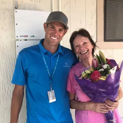 Ben from Burmax Energy with a happy customer holding flowers beside her new SolarEdge inverter
